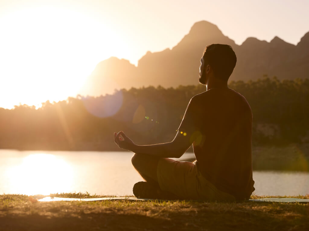 Person meditating peacefully by lake at dawn