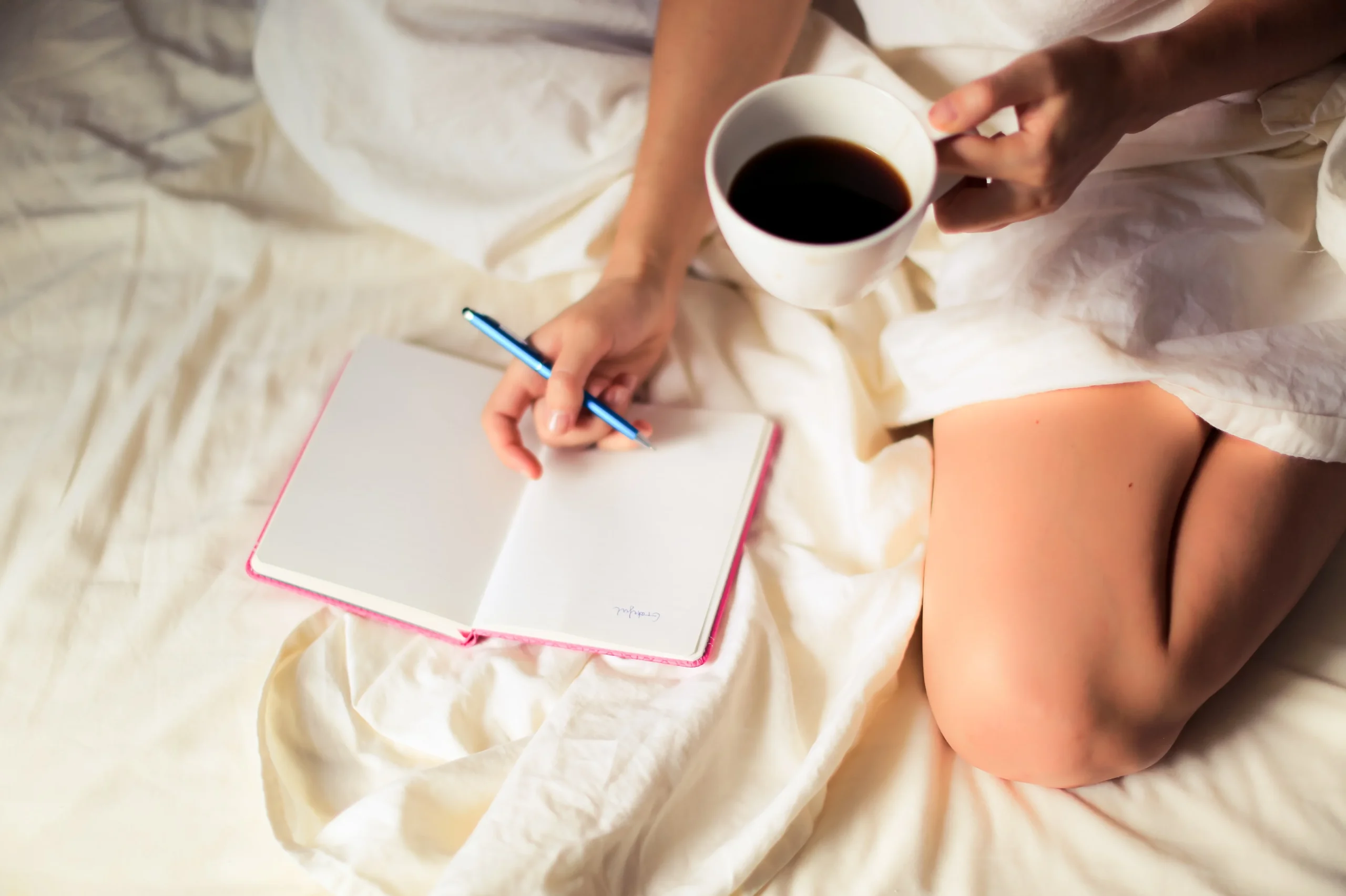 Journal, pen and coffee on bed in pool of morning sunlight